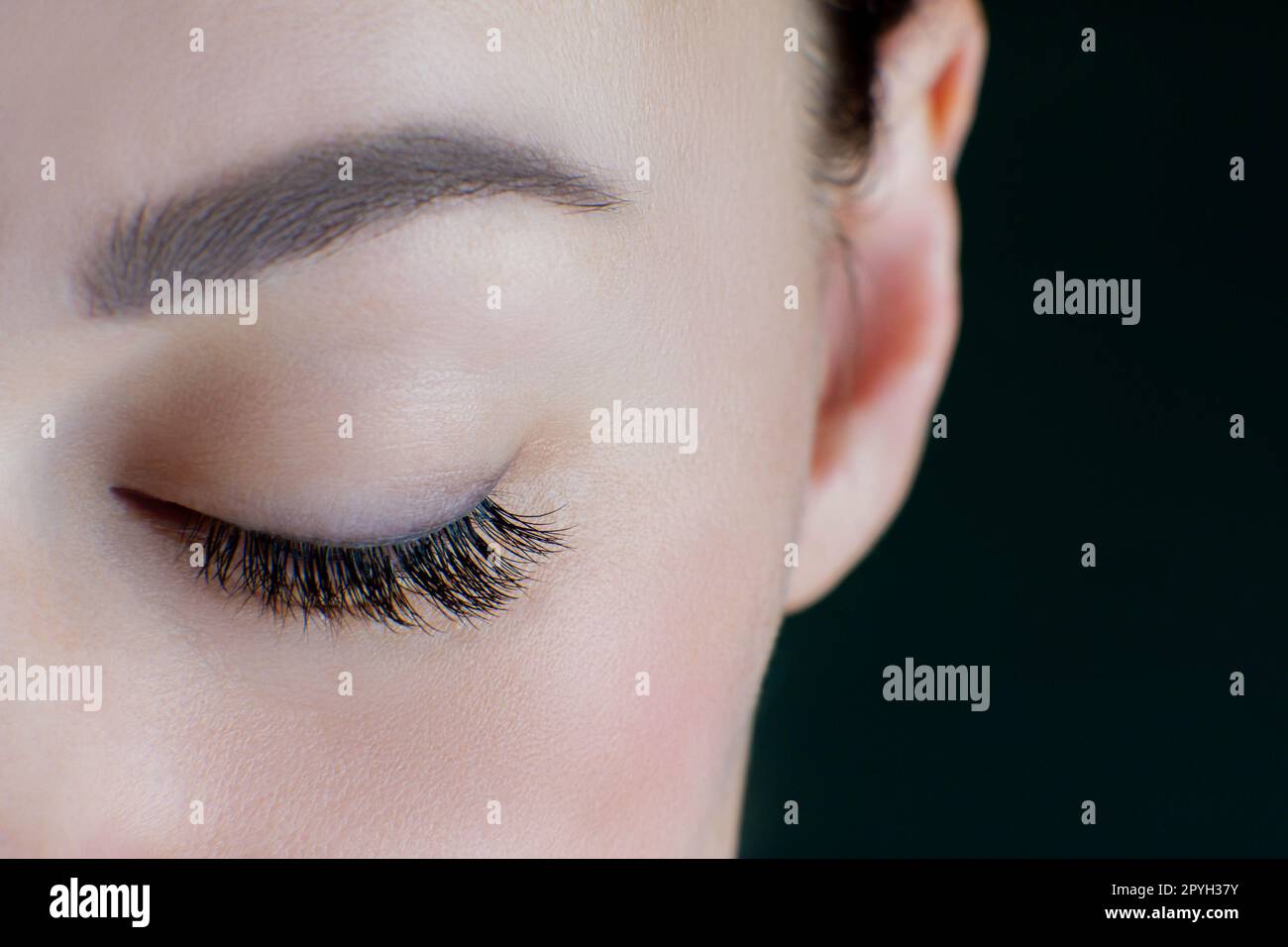 Close-up of closed eye with amazing long eyelashes, black eyeliner, perfect skin, eyebrow of unrecognizable young woman. Stock Photo