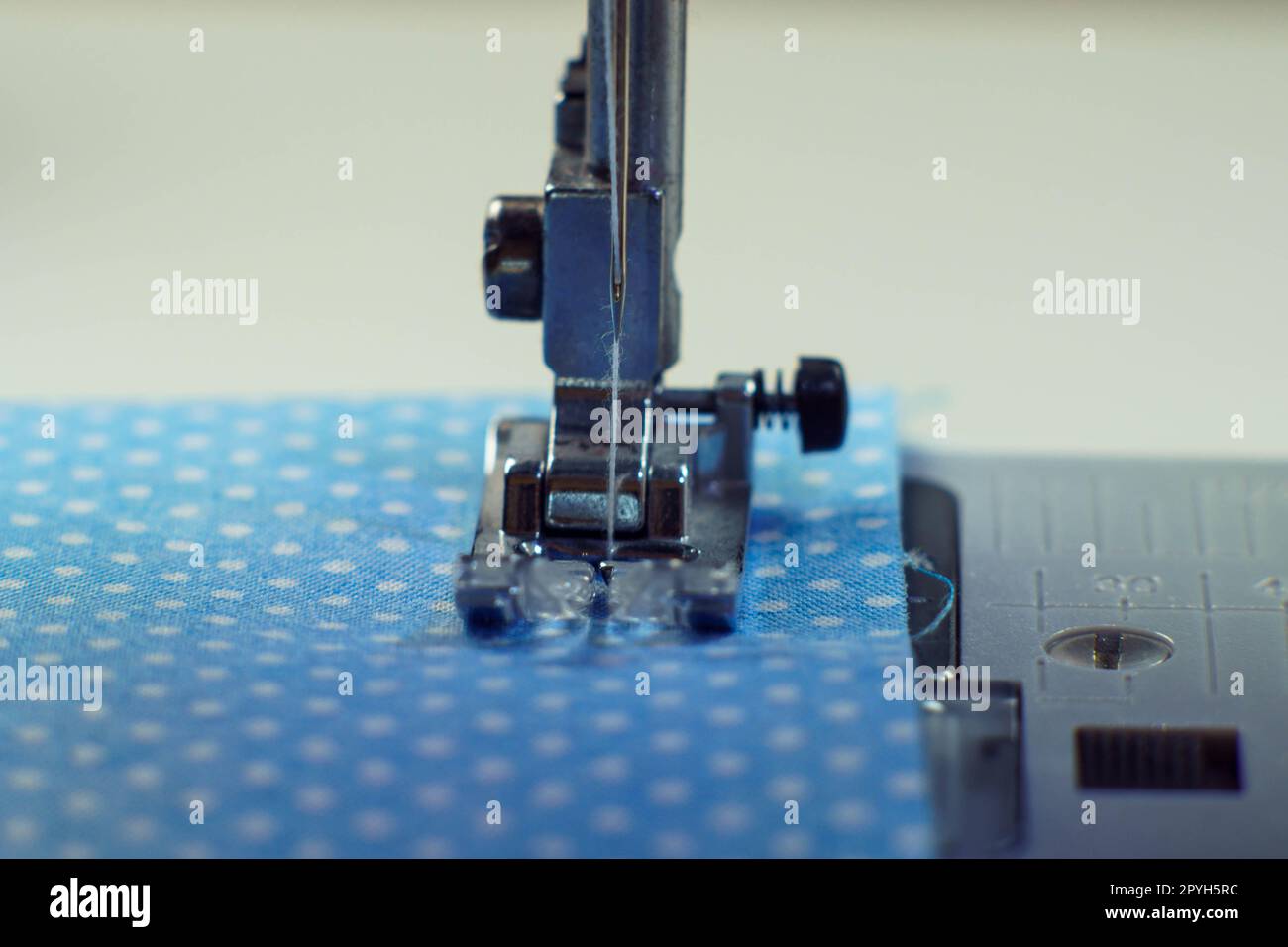 Detailed close up shot of sewing machine steel foot with needle and thread stitching on blue fabric polka dot textile Stock Photo