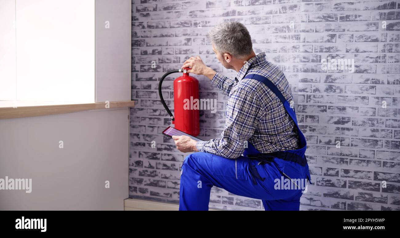 Worker Installing Fire Extinguisher. Inspection Service Stock Photo