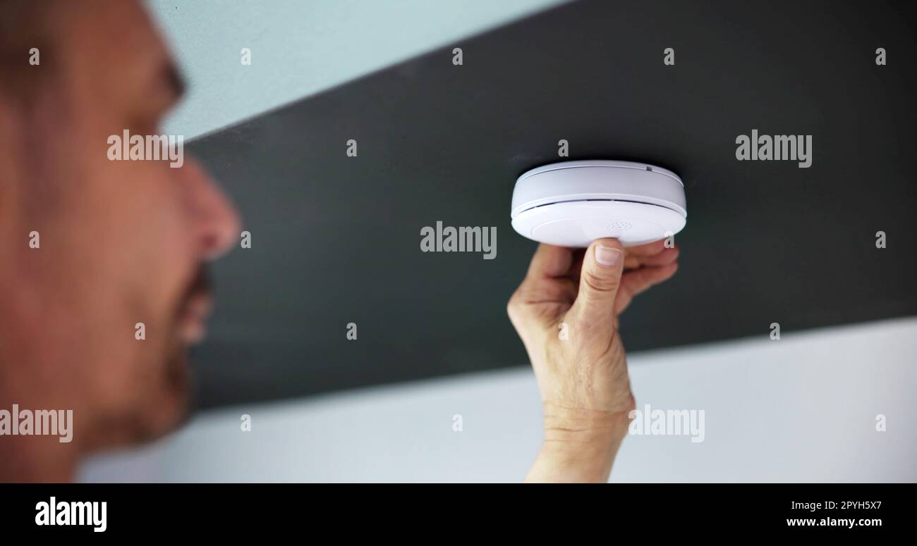 Person's Hand Installing Smoke Detector On Ceiling Wall Stock Photo