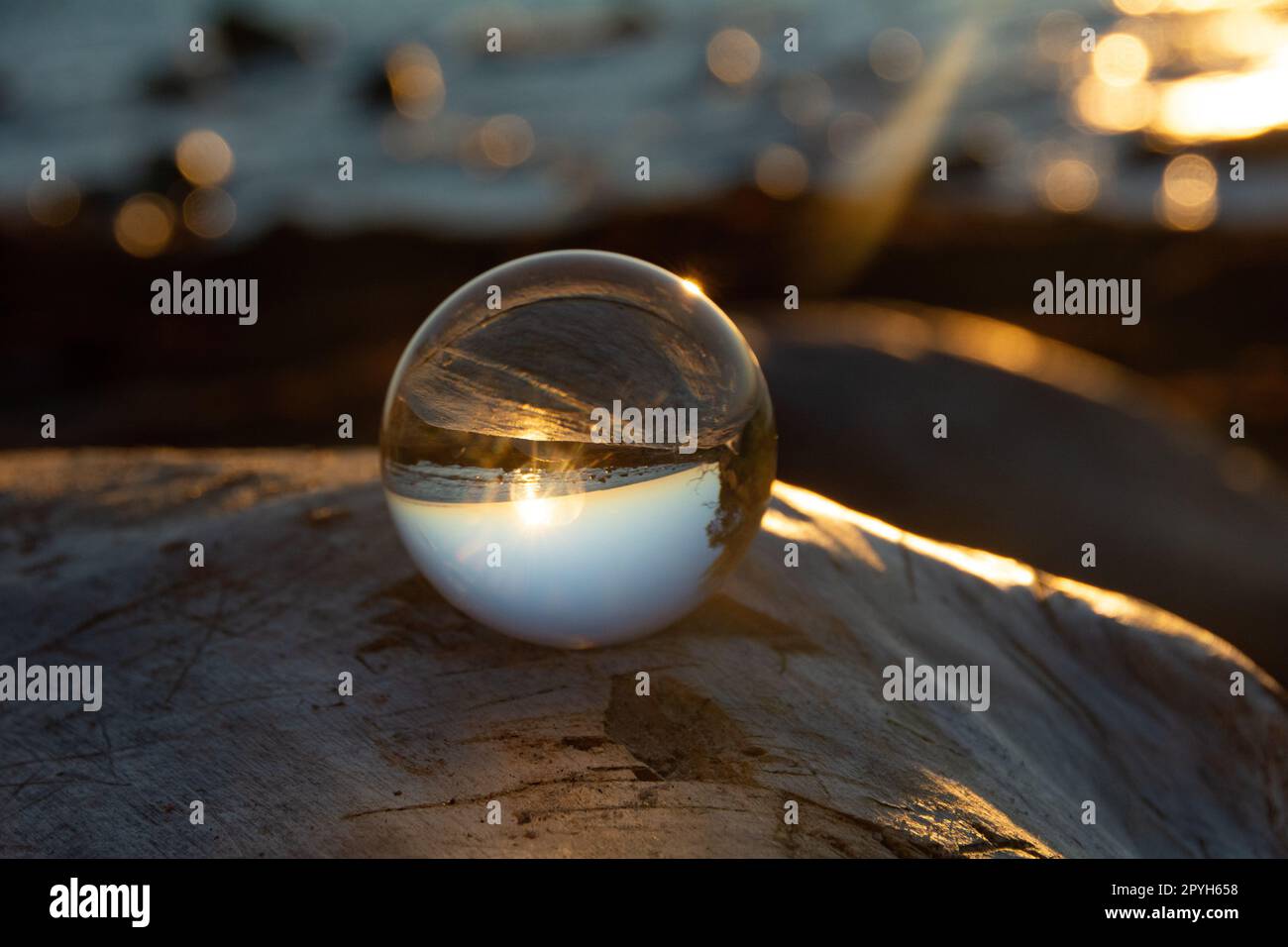 Ball made of glass lies on a stone in which the beach and the sea are ...