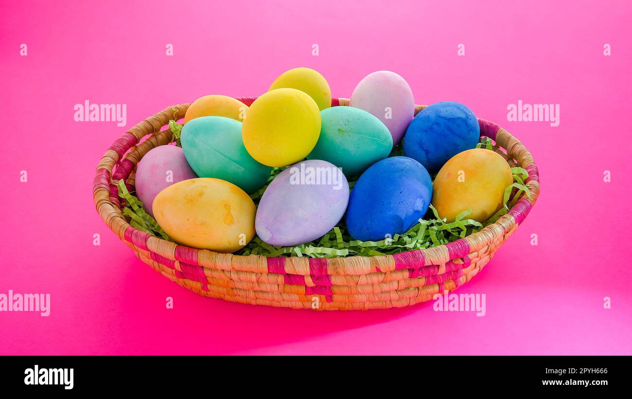 Colorful bright  Easter eggs inside basket on pink background Stock Photo