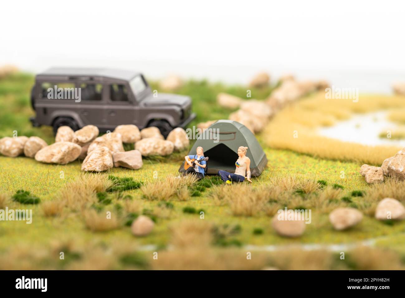 Miniature man playing guitar with his friend at campsite Stock Photo