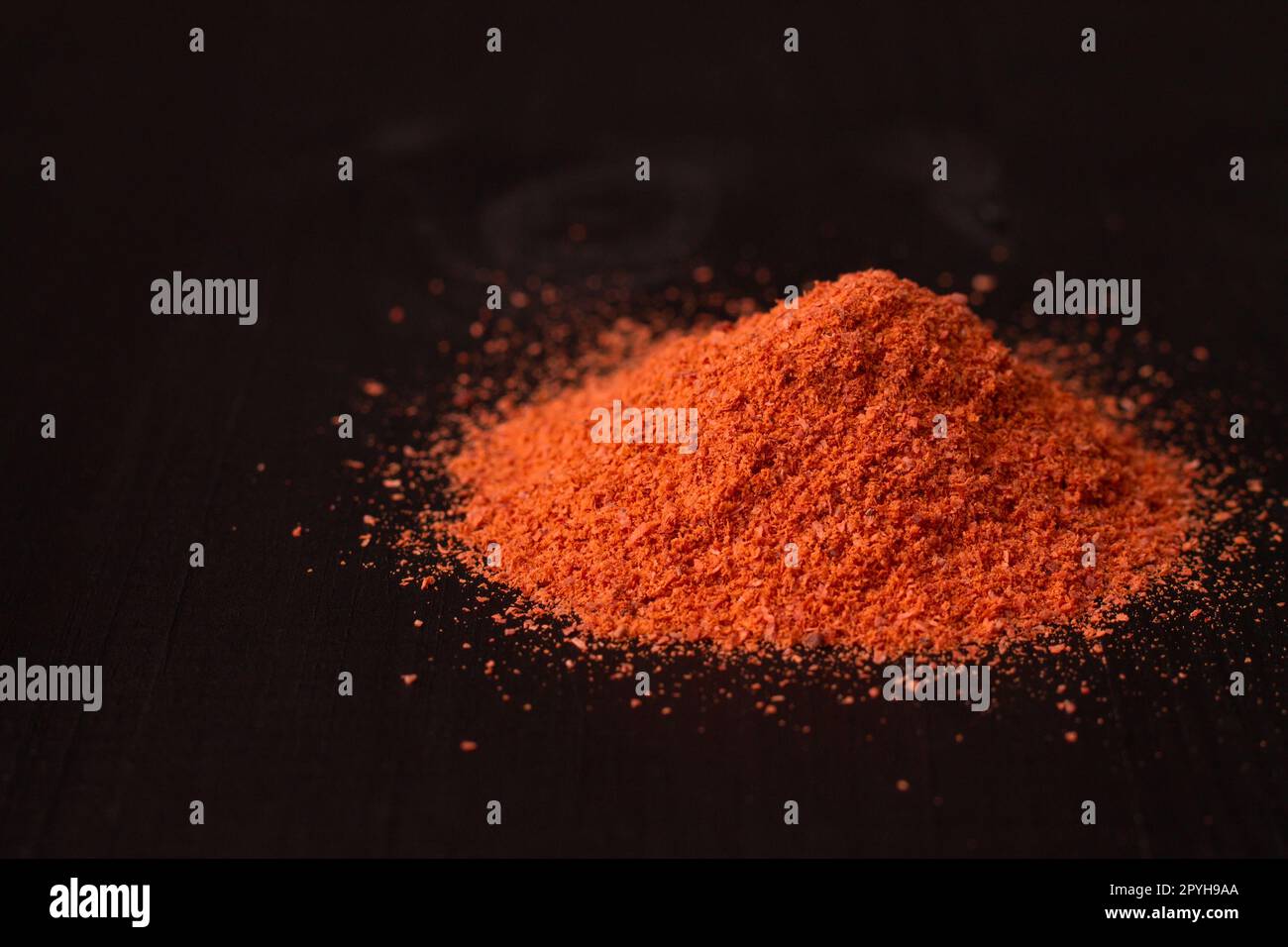 A pile of red hot pepper powder on a black wooden surface. Copy space Stock Photo