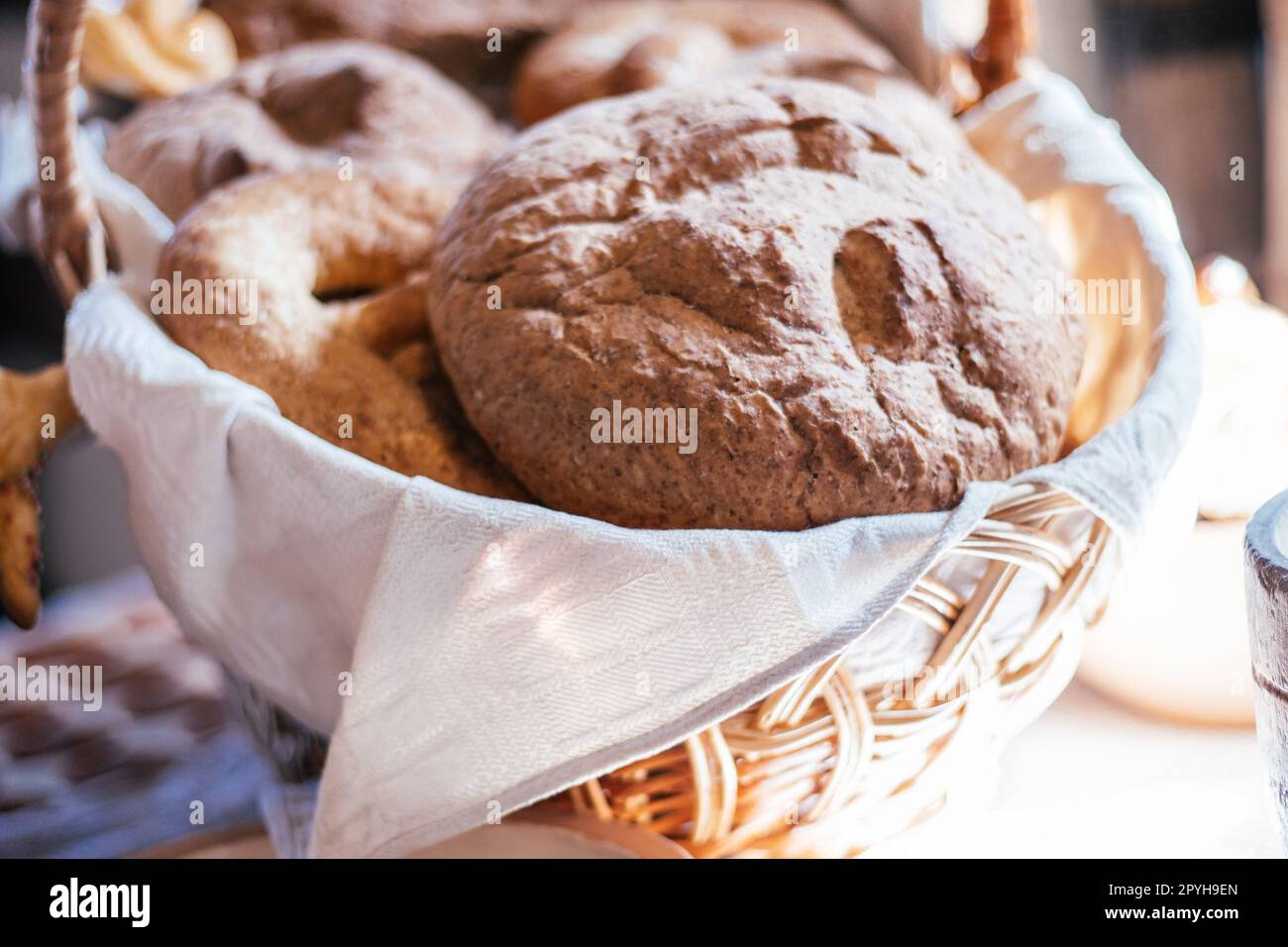 Delicious gourmet fresh baked goods buns, pone, fancy rye bread, pastry in napkin woven basket on blurred background. Stock Photo
