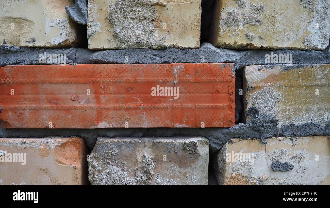 Brick wall. Ceramic masonry or fence. Old, uneven brick, covered in moss and mold in some places. The texture of the stone or mineral. The effect of moisture on brick structures. Village motifs. Stock Photo