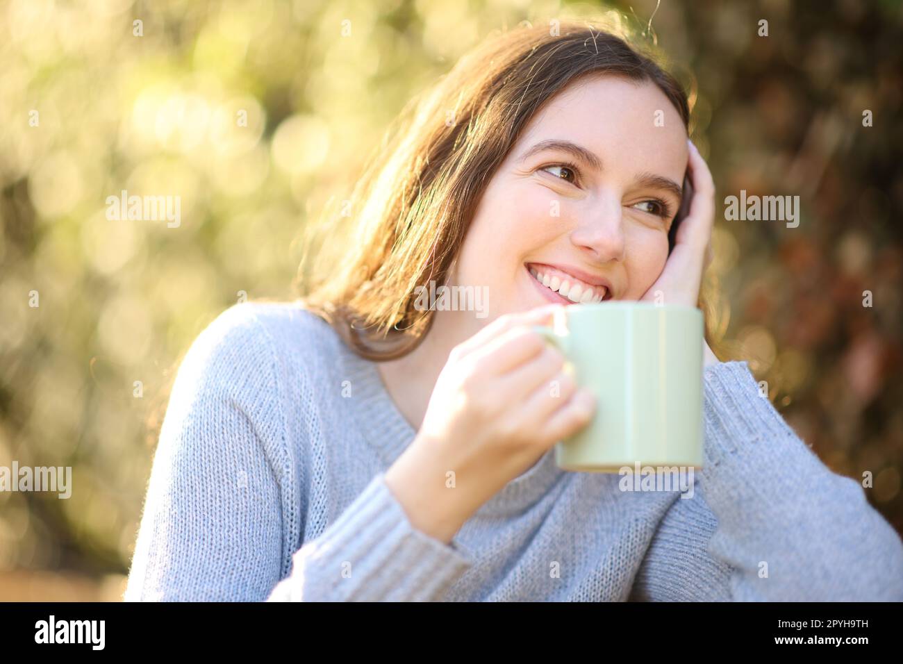 Happy woman drinking coffee in a park looking away Stock Photo