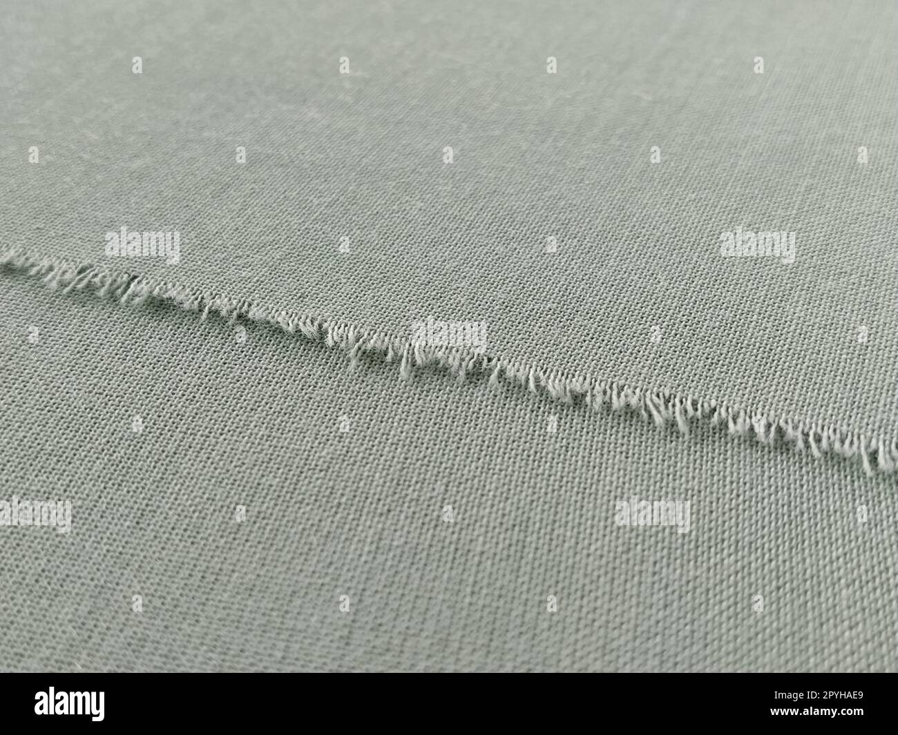 Ripped edge of fine woolen fabric in green or blue. Loose threads at ...