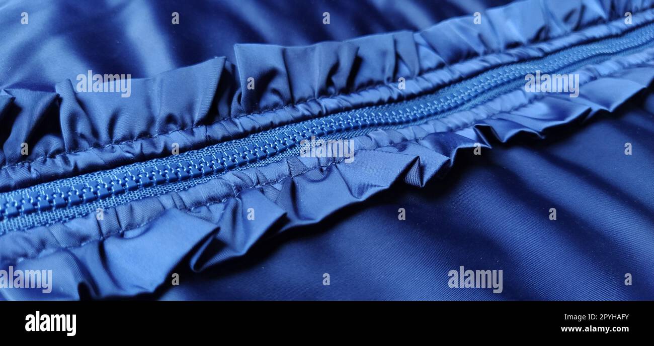 Buttoned zip on a blue raincoat. Waves and folds in the fabric. Beautiful flounces, ruffles, frills. Decorative finishing of a garment. Smocked, sewn silk fabric. Nice casual wear. Stock Photo
