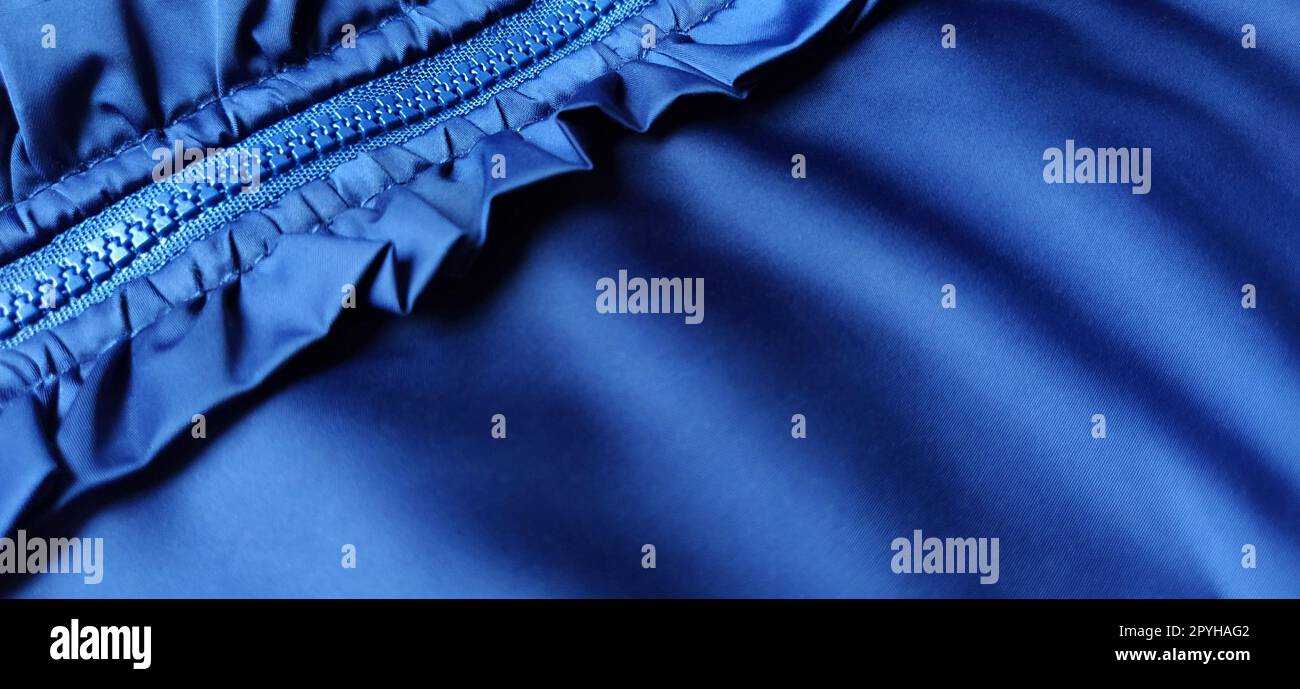 Buttoned zip on a blue raincoat. Waves and folds in the fabric. Beautiful flounces, ruffles, frills. Decorative finishing of a garment. Smocked, sewn silk fabric. Nice casual wear. Stock Photo