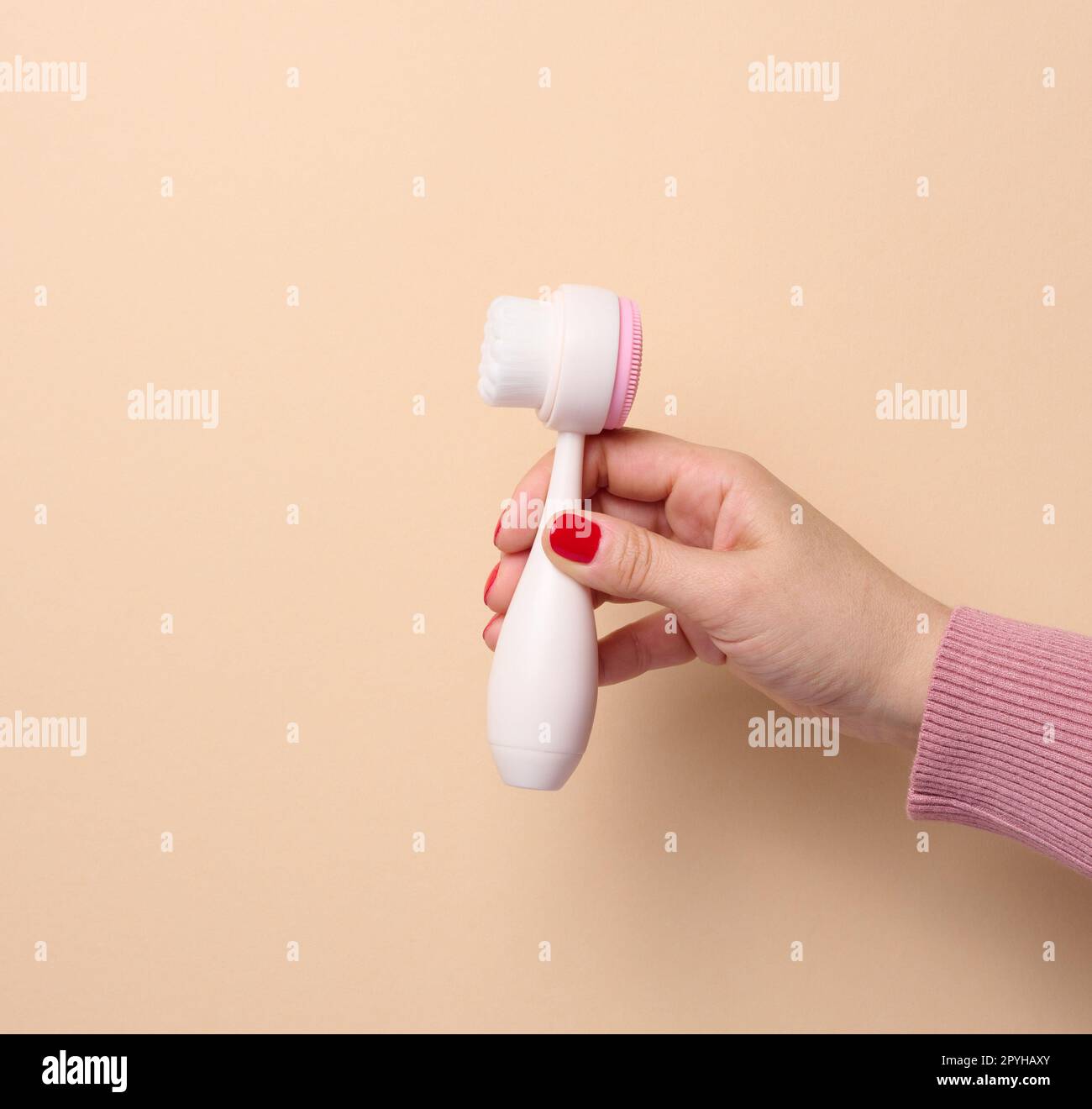 A woman's hand holds a plastic brush for face and body on a beige background Stock Photo