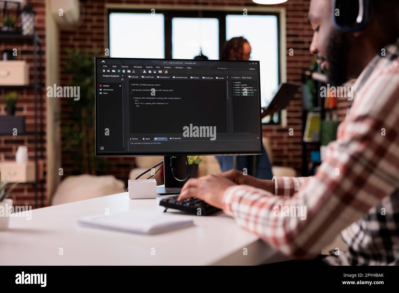 Freelance programmer with wireless headphones writing code on personal computer while girlfriend is using laptop standing in living room. African american man developing software debugging algorithm. Stock Photo