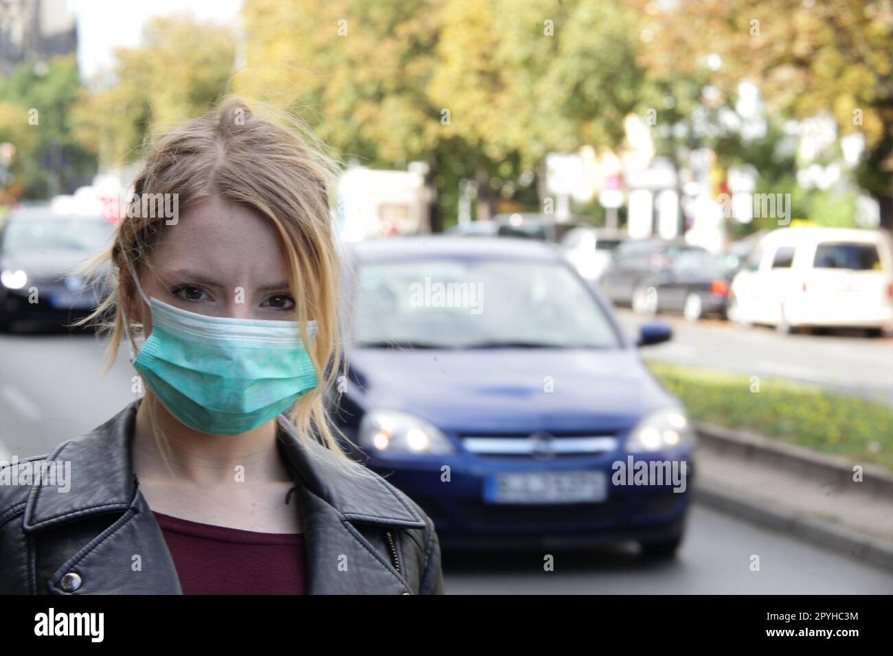 junge frau mit mundschutz auf der straße schützt sich im straßenverkehr gegen die autoabgase Stock Photo