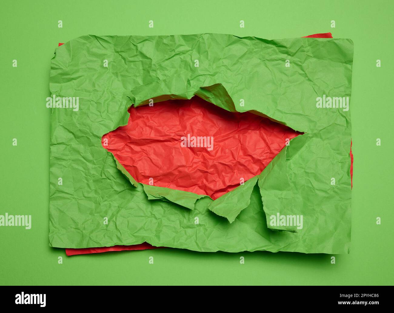 Texture of crumpled green paper with torn hole and red background Stock Photo