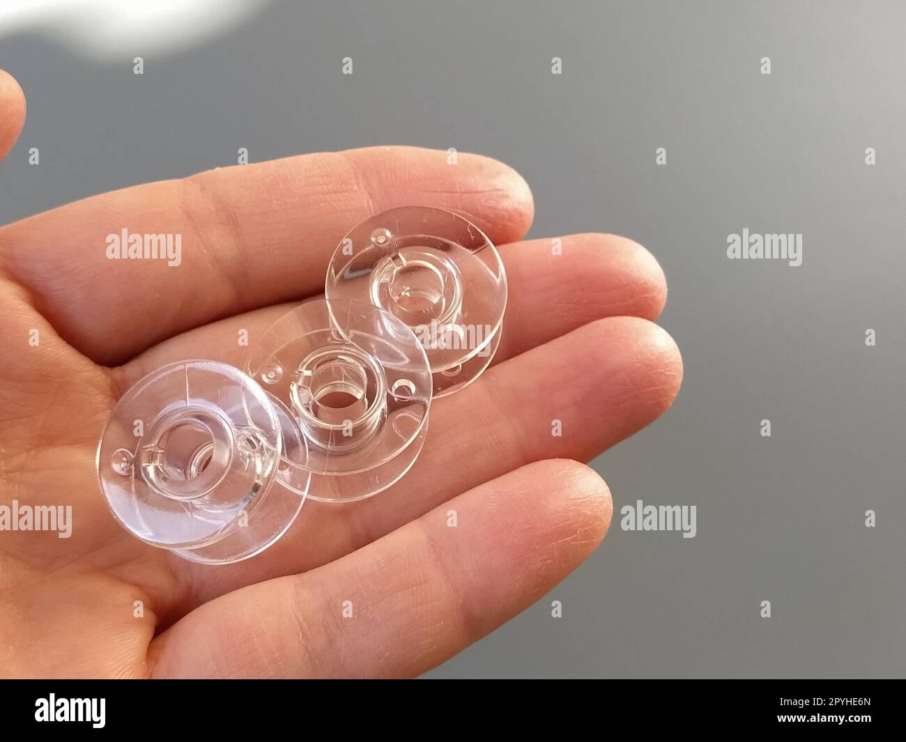 Transparent plastic bobbins from a modern sewing machine in the palm of a woman - a seamstress. Gray background. sewing machines Stock Photo