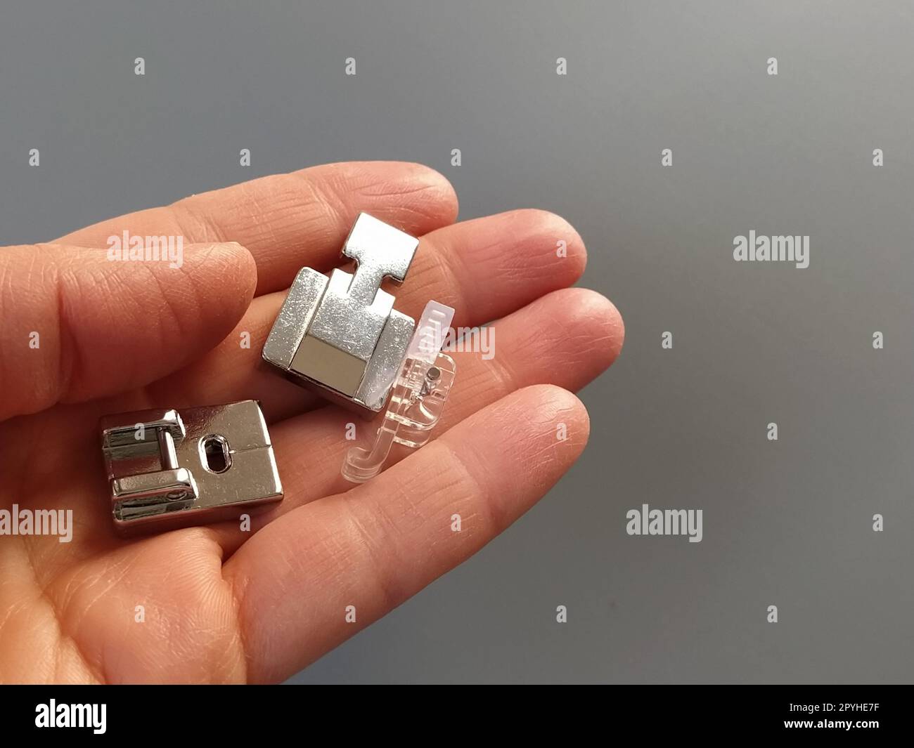 A set of feet for an electric sewing machine in a female hand. Gray