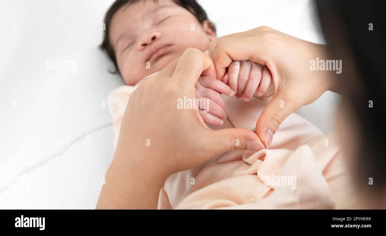Mother holding hands of her newborn baby on white bedding Stock Photo