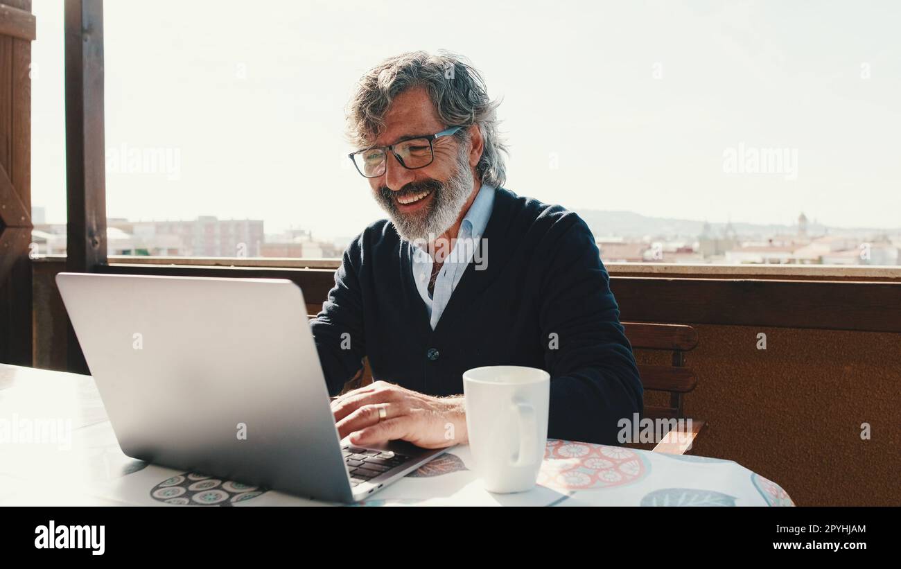 Happy middle aged man communicates remotely using laptop. Working from home office Stock Photo