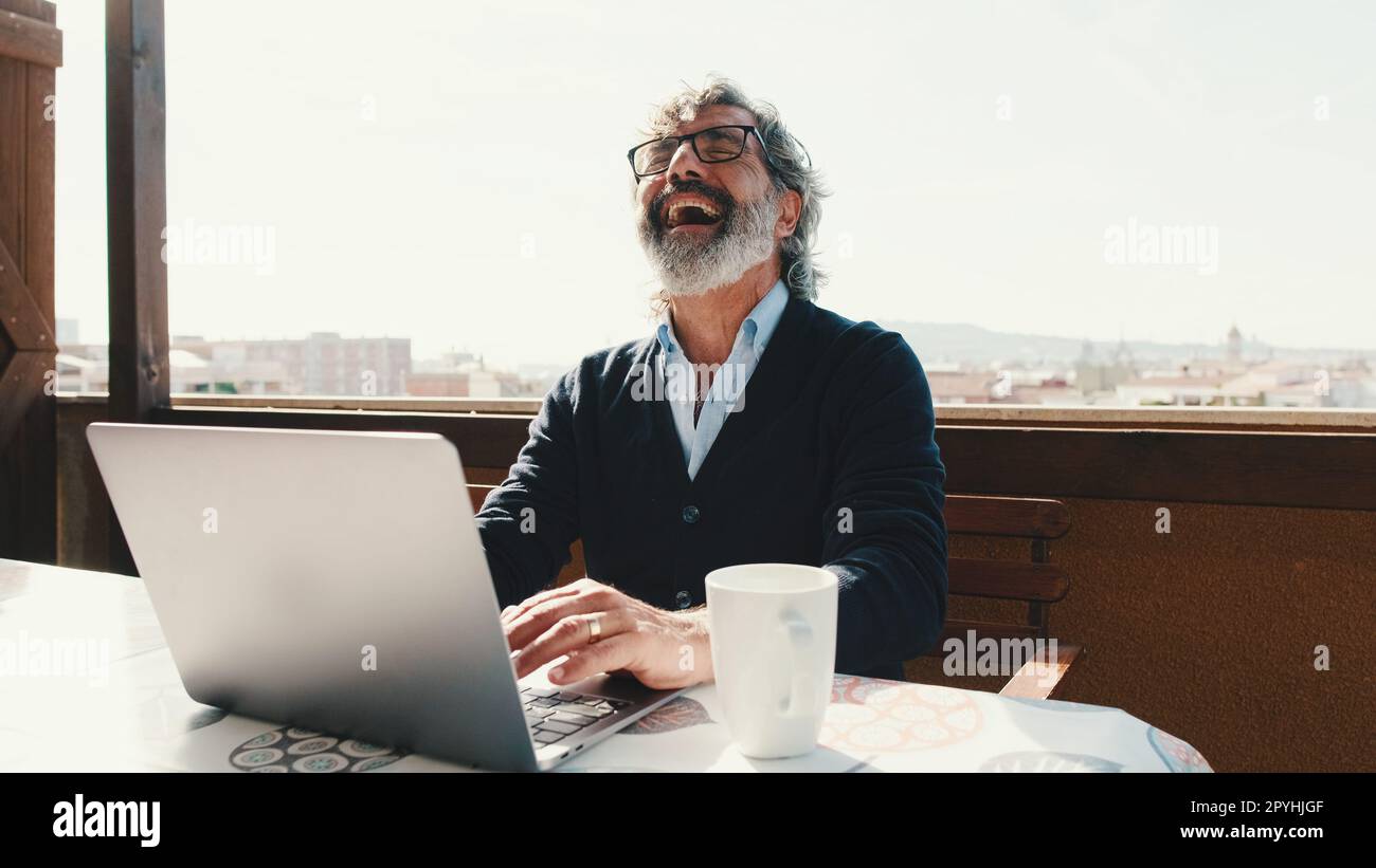 Happy middle aged man communicates remotely using laptop. Working from home office Stock Photo