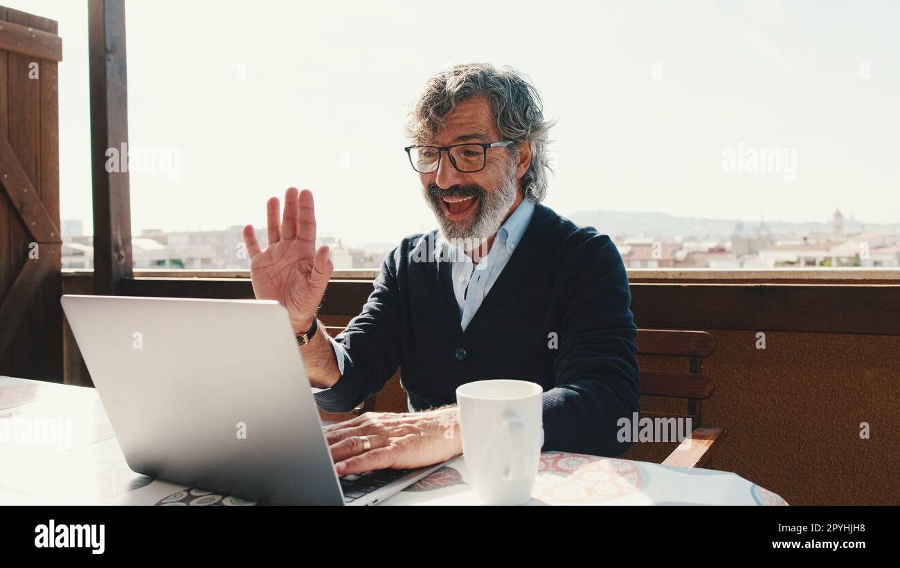 Happy middle aged man communicates remotely using laptop. Working from home office Stock Photo