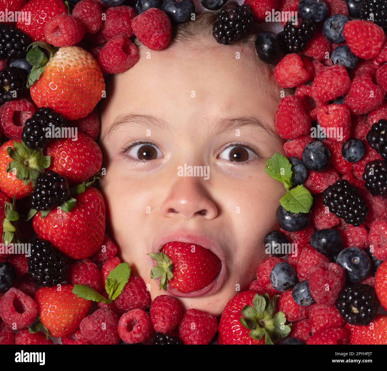 Summer fruits. Child face with berries mix of strawberry, blueberry