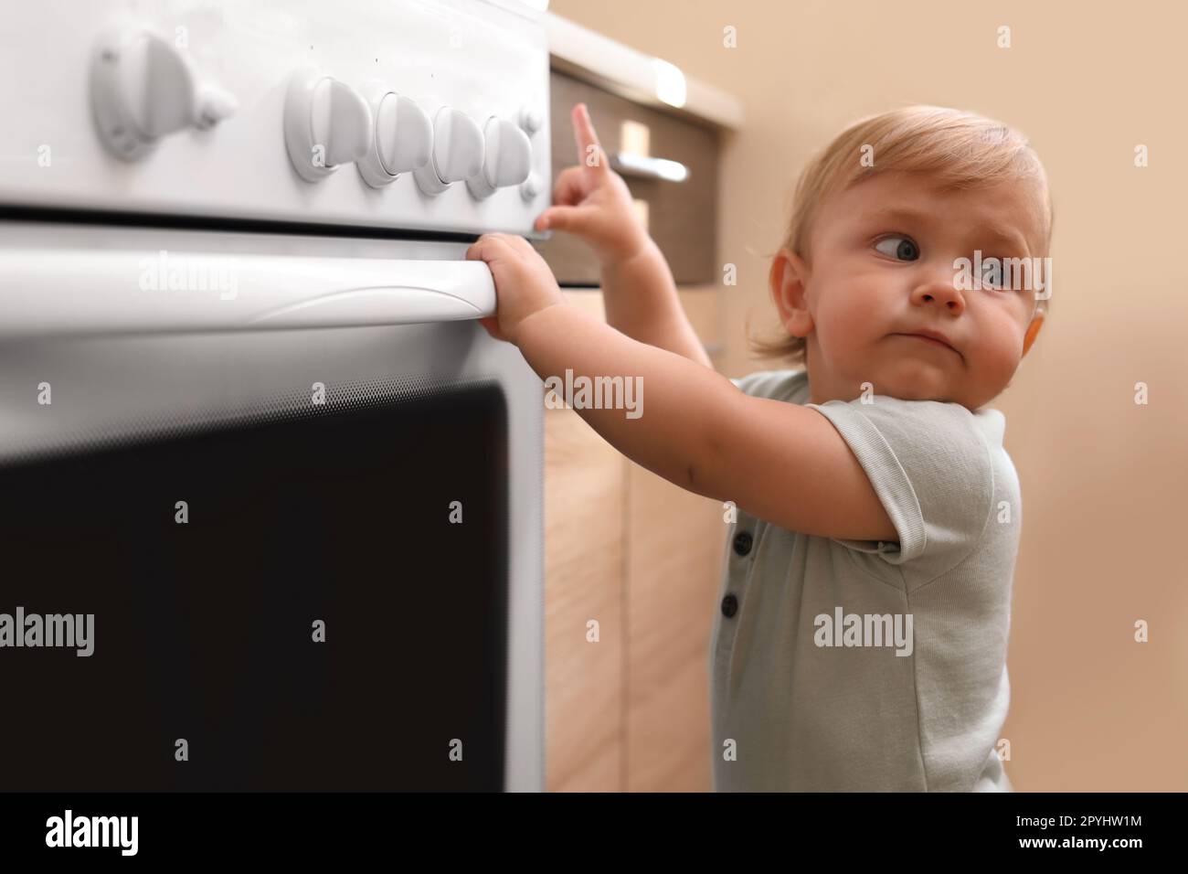 Little child playing with gas stove indoors. Dangers in kitchen Stock