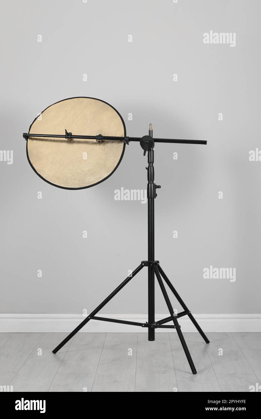 Studio reflector on tripod near grey wall indoors. Professional