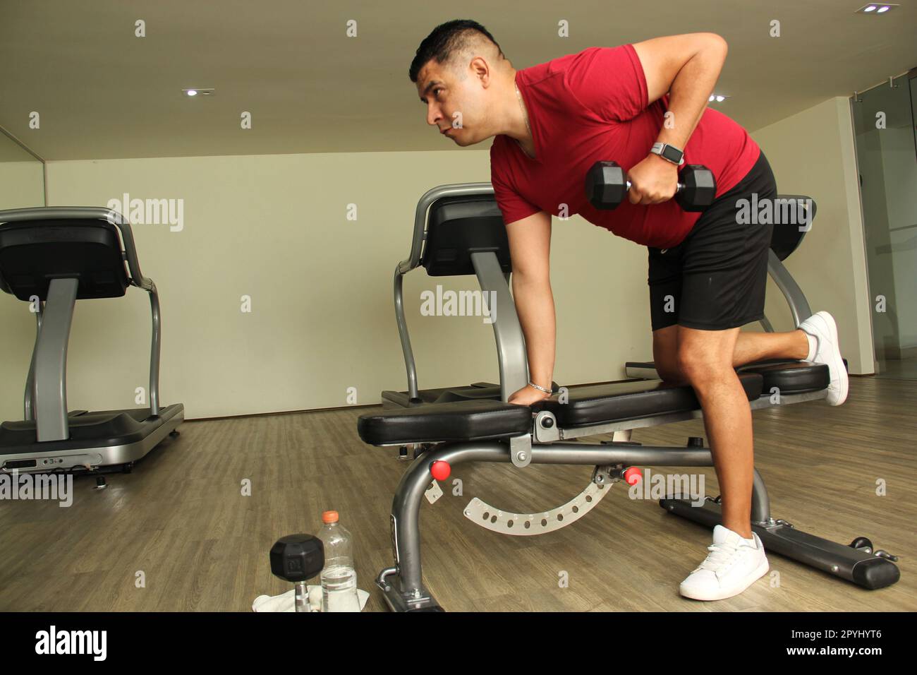 Dark-haired latino adult man exercises in a gym, muscle strength work for physiotherapy rehabilitation on arm with dumbbells Stock Photo