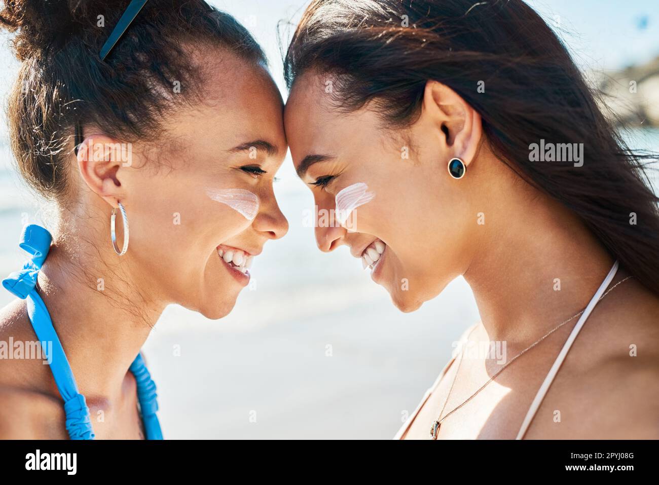 UV got a friend in me. two beautiful young women at the beach with sunscreen on their faces smiling at each other. Stock Photo