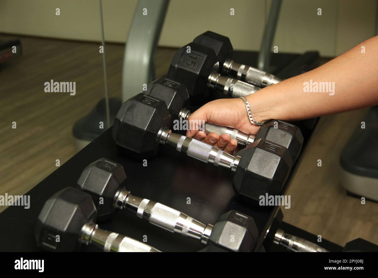 Dark-haired latino adult man exercises in a gym, muscle strength work for physiotherapy rehabilitation on arm with dumbbells Stock Photo