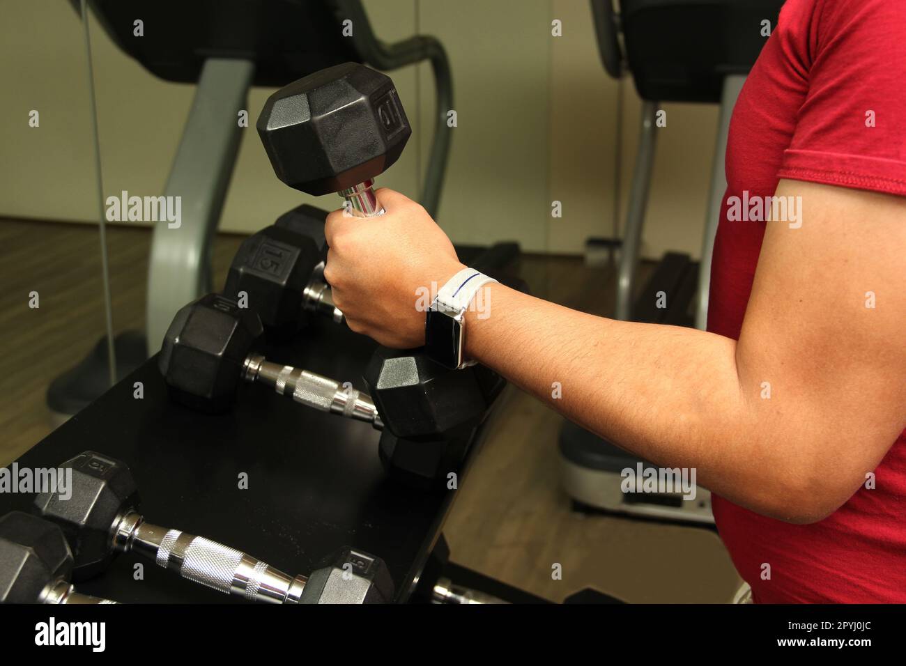 Dark-haired latino adult man exercises in a gym, muscle strength work for physiotherapy rehabilitation on arm with dumbbells Stock Photo