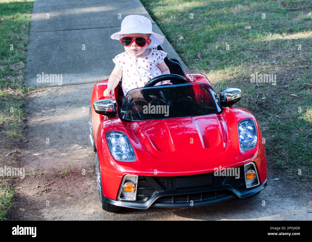 Caucasian baby in white hat riding in an electric convertible red sport car. child driving a car on a summer day Stock Photo