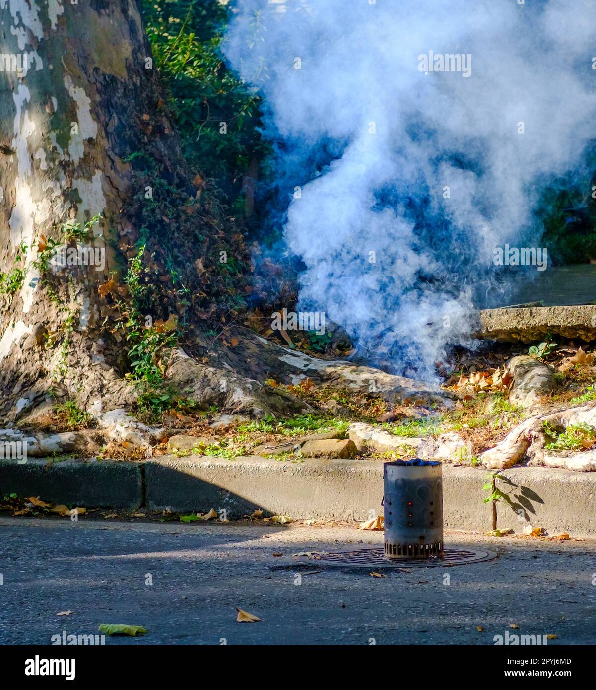 Chimney charcoal starter, with fire and smoke, left on a manhole cover