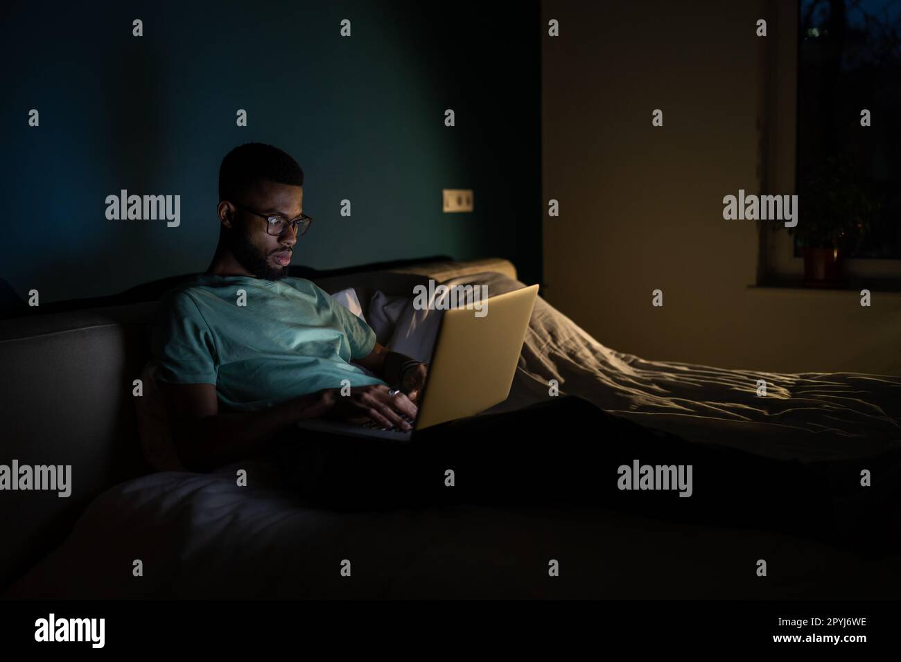 Black guy freelance IT developer using laptop at night, coding until late hours to meet deadline Stock Photo