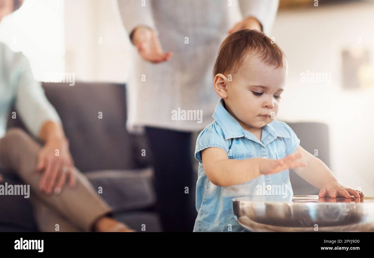 Busy hands are learning hands. an adorable baby girl banging playfully on a table with her family in the background. Stock Photo