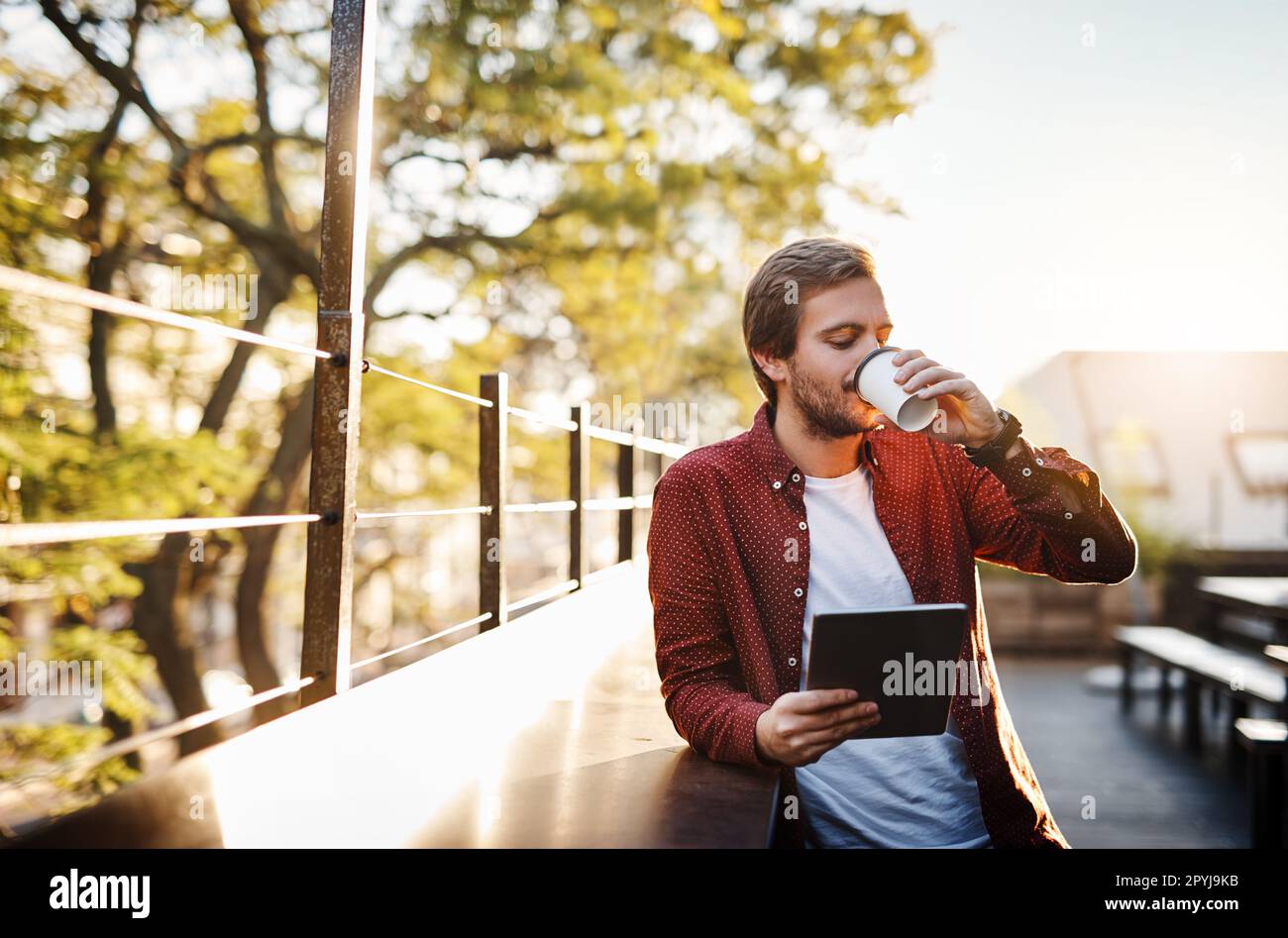 Coffee and connectivity. a handsome young man using his digital tablet while drinking coffee outside. Stock Photo