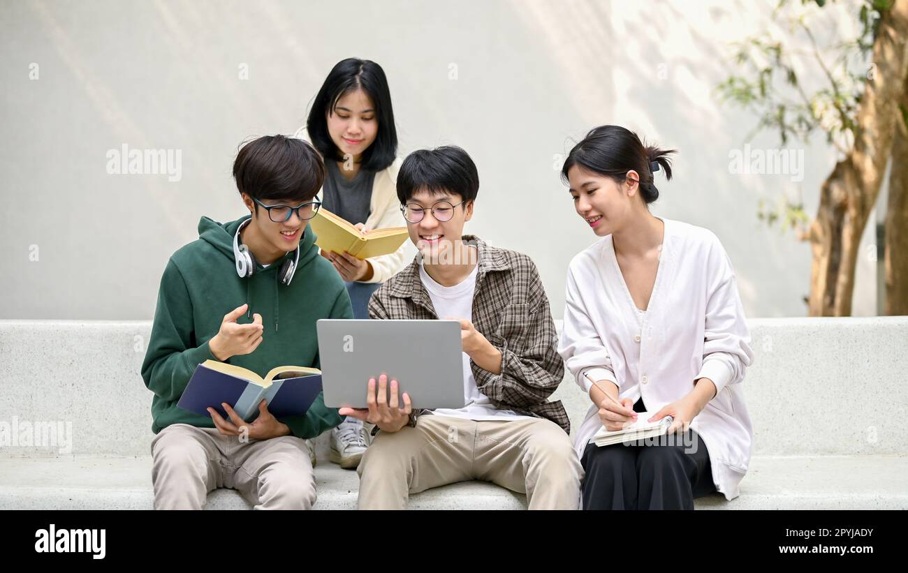Group of happy young Asian college students sitting on a bench, looking ...