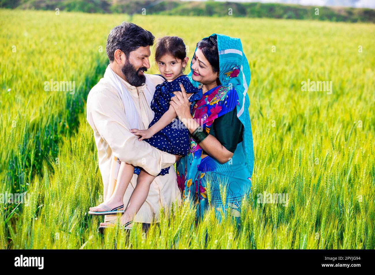 Portrait of happy young indian farmer family standing at wheat ...
