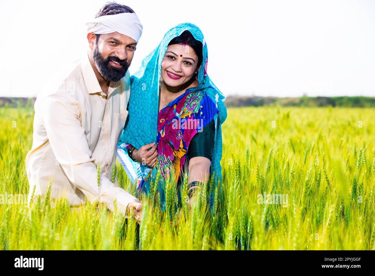 Portrait of happy young indian farmer couple touching wheat crop ...