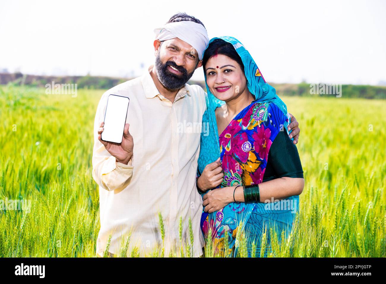 Happy young indian farmer couple showing smart phone with blank display ...