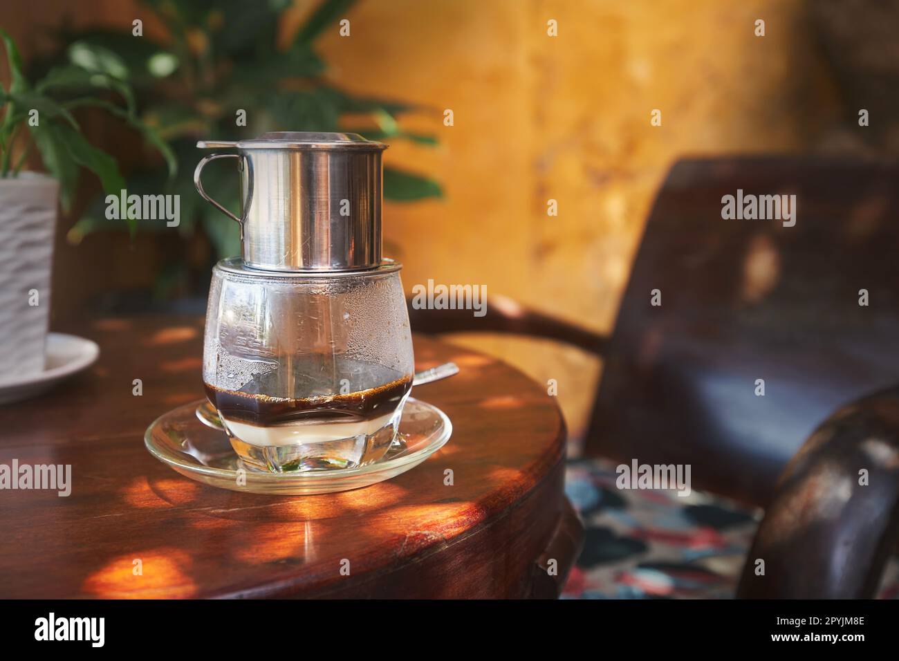 Glass of traditional hot Vietnamese coffee with condensed milk on wooden table in cafe in