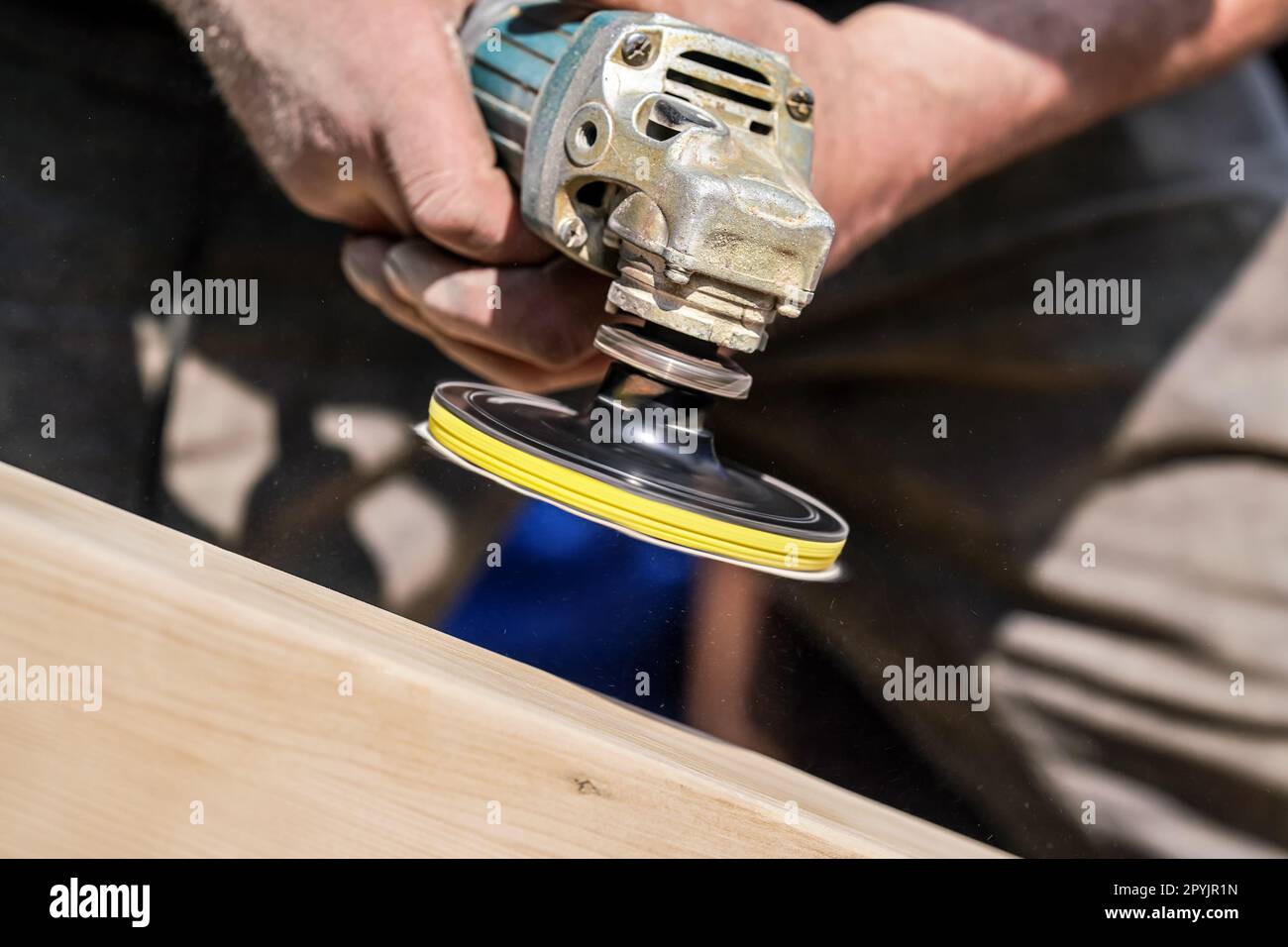 Man polishing wooden chest with old angle grinder during sunny day, closeup detail to hands without gloves, fine wood dust flying in air Stock Photo