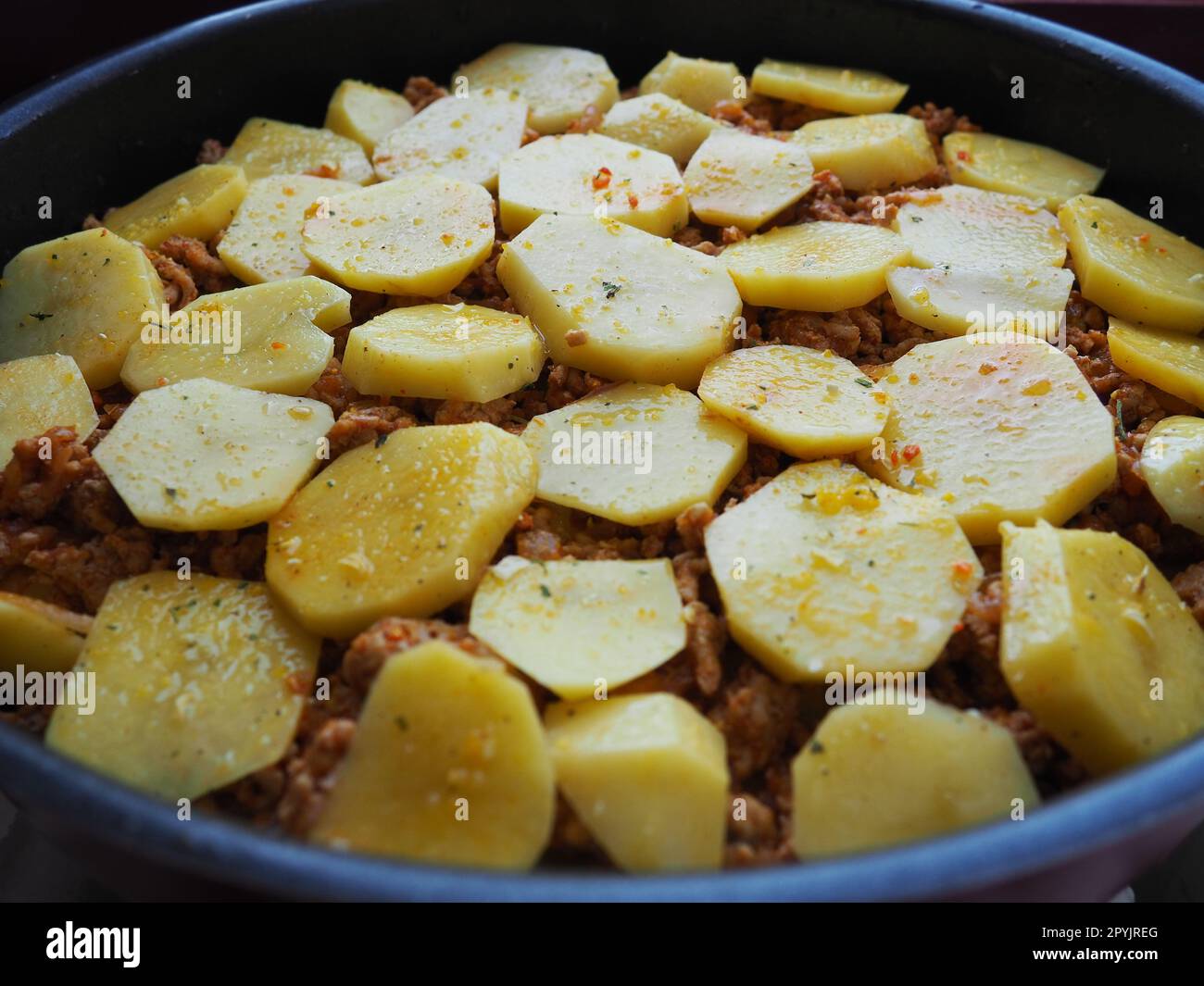 Raw potatoes, cut into circles and stacked on top of minced meat and onions. Moussaka making process. Spices on potatoes. Balkan cuisine - traditional Greek, Serbian and Turkish food Stock Photo