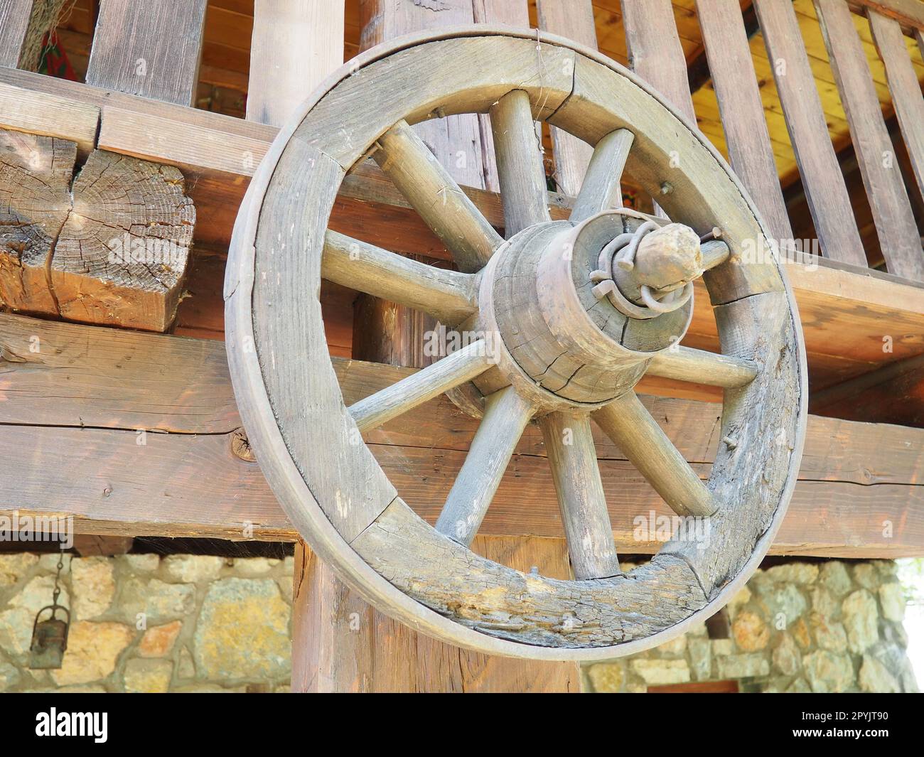 Wooden wheel from a cart. Decorative wheels for decorating lawns, exteriors and rustic interiors. A round homemade wheel hangs on the wall. Retro or vintage style. Life in the countryside Stock Photo