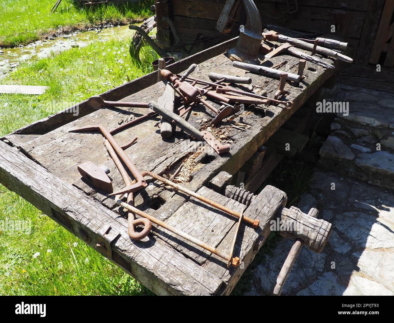 vintage working tools on a wooden table. Wooden and metal tools for building and rural life. Hammer, bracket, saw, ax, drill, tongs, poker, spoon, wooden vice. Village life. Joinery and carpentry Stock Photo