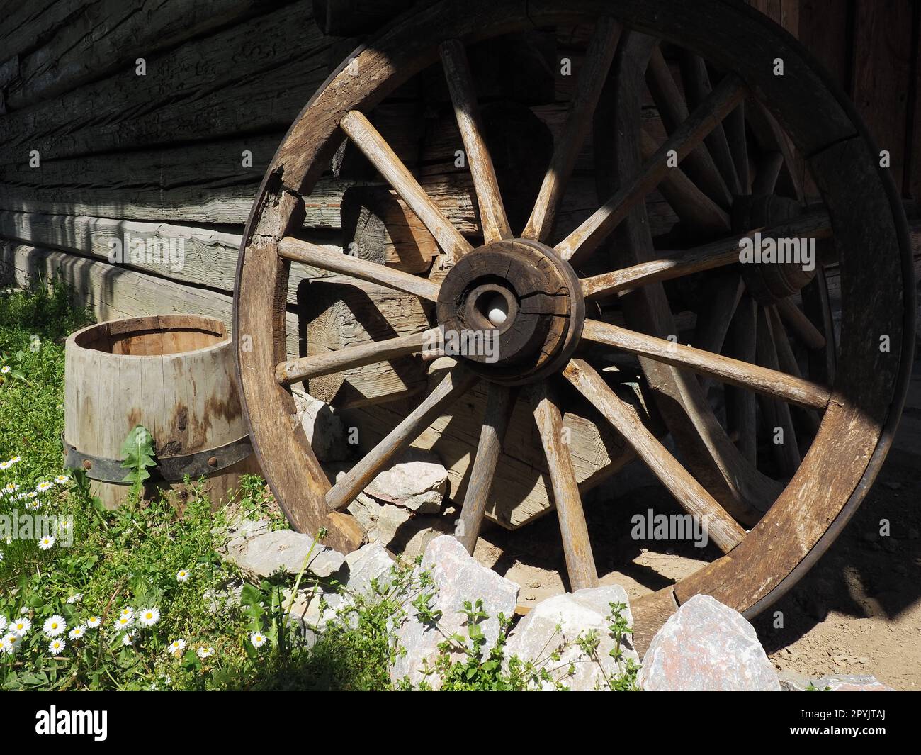 Wooden wheel from a cart. Decorative wheels for decorating lawns, exteriors and rustic interiors. Round homemade wheel against the wall. Retro or vintage style. Life in the countryside Stock Photo