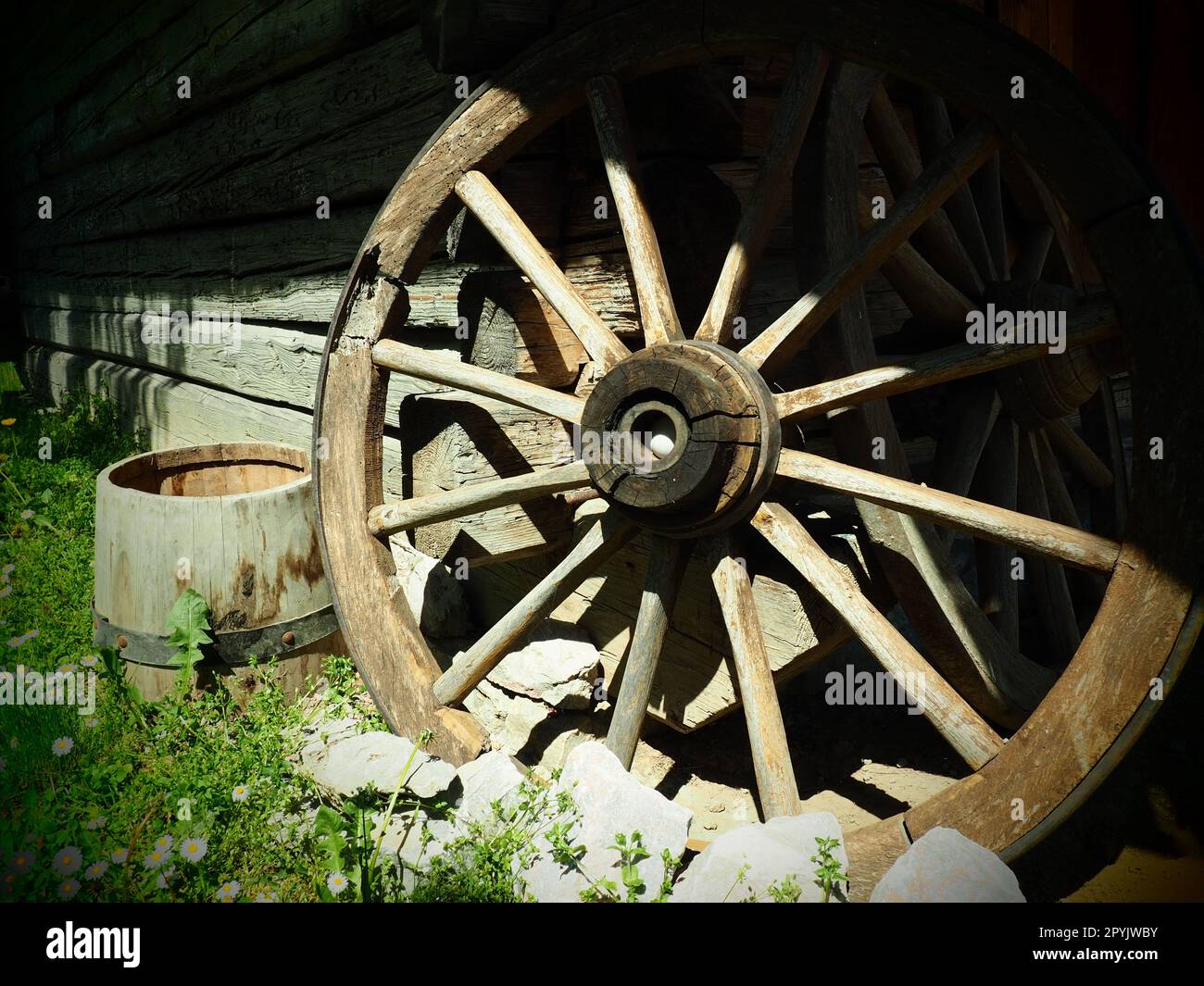 Wooden wheel from a cart. Decorative wheels for decorating lawns, exteriors and rustic interiors. Round homemade wheel against the wall. Retro or vintage style. Life in the countryside Stock Photo