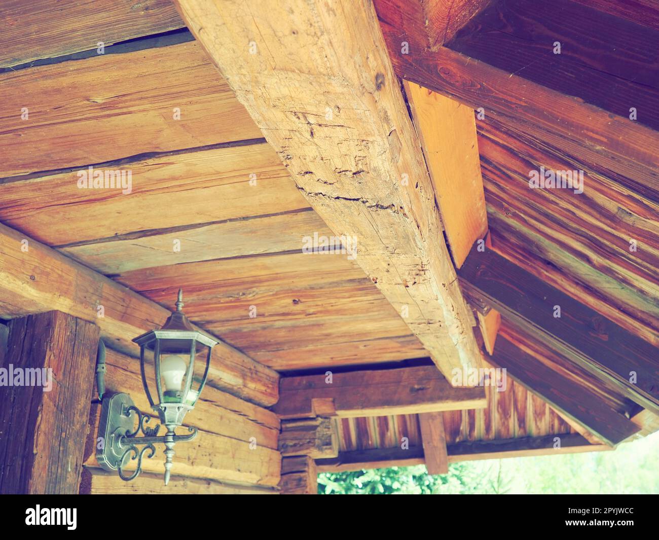 Woodworking for construction and roofing. Wooden beam and roof in a traditional peasant house. Metal lantern on the wall. Wooden architecture. Stanisici, Bijelina, Bosnia and Herzegovina. Stock Photo