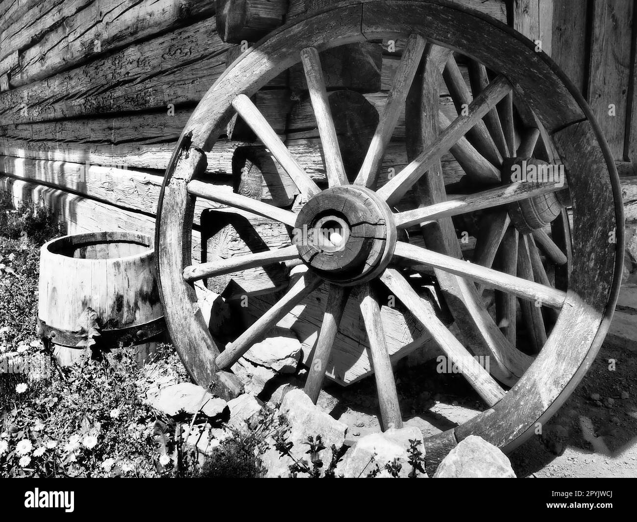 Wooden wheel from a cart. Decorative wheels for decorating lawns, exteriors and rustic interiors. Round homemade wheel against the wall Retro or vintage style. Life in the countryside. Black and white Stock Photo
