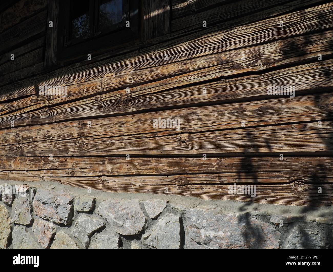 Log wooden wall of an old village house. Cobblestone foundation. Old methods of construction of residential buildings. Stock Photo